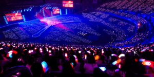 K-pop Idol System concert stadium filled with fans holding colorful lightsticks at a major idol group performance, showcasing the massive scale of K-pop fandom compared to Hollywood celebrity events