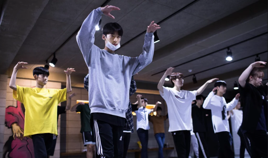 K-pop Trainee System: Young performers practicing intense dance choreography in a training studio, showcasing the rigorous idol development process