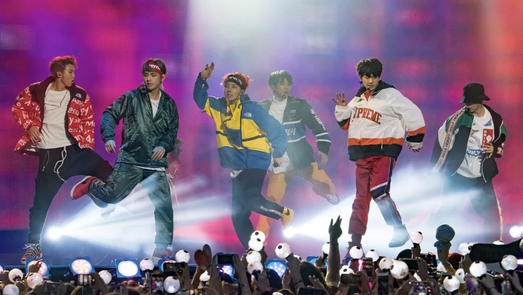 K-pop concert evolution showcased through dynamic BTS stadium performance with synchronized choreography and illuminated light sticks creating an immersive fan experience