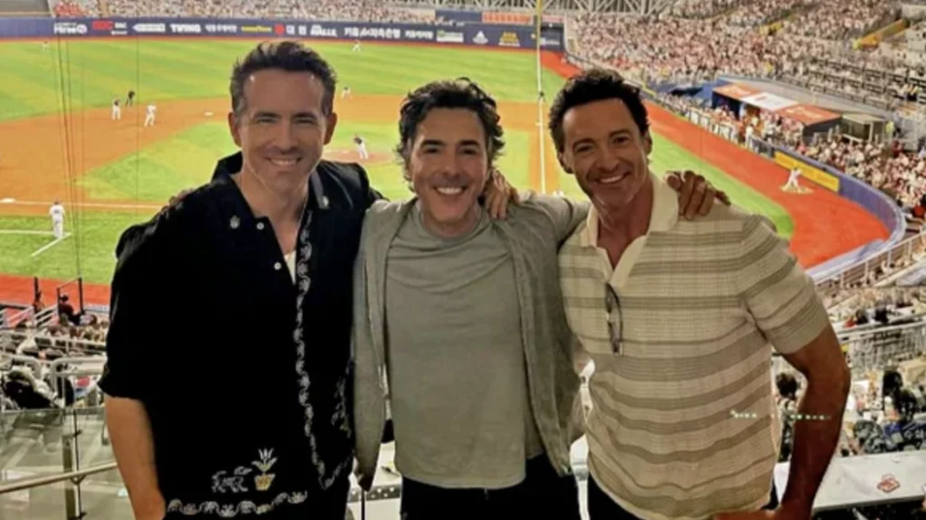 Hollywood stars enjoying a KBO League baseball game at Gocheok Sky Dome in Seoul, with the packed stadium visible in the background. The three men are smiling for a photo while experiencing Korean baseball culture during their visit to Korea. The stadium shows the impressive attendance and atmosphere that makes Korean baseball famous internationally, highlighting how the KBO attracts celebrity visitors who are often amazed by the unique and energetic fan experience.
