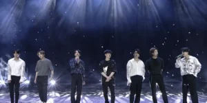 BTS seven members standing together on stage with dramatic blue lighting and falling snow effects during their comeback performance, showcasing their reunion after military service completion