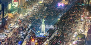 Aerial night view of massive K-protest culture demonstration in Seoul featuring thousands of peaceful protesters with light sticks creating a festival-like atmosphere around Gwanghwamun Square