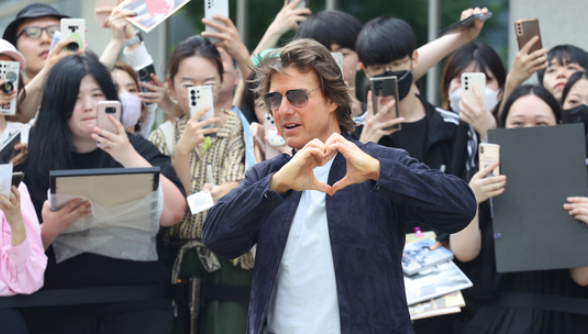 Tom Cruise making heart gesture during Korea Visit for Mission Impossible 8 while surrounded by enthusiastic Korean fans taking photos