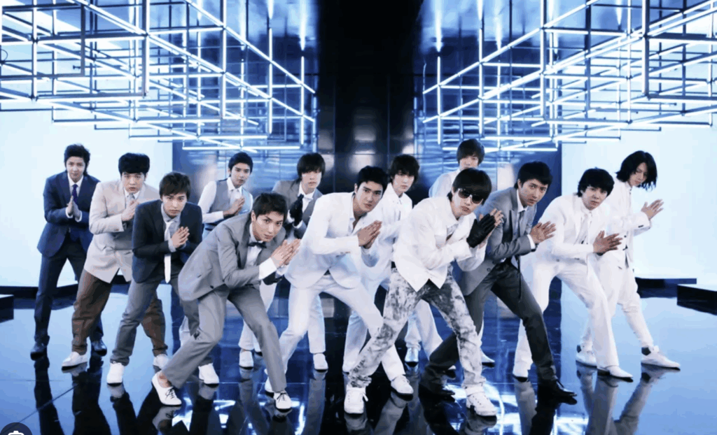 Super Junior performing their iconic Sorry Sorry choreography in matching formal suits during a music video shoot with dramatic blue lighting and geometric stage design
