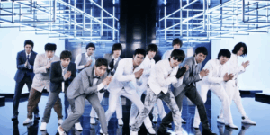 Super Junior performing their iconic Sorry Sorry choreography in matching formal suits during a music video shoot with dramatic blue lighting and geometric stage design