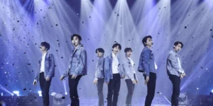 ENHYPEN fourth generation kpop leaders performing on stage during Walk the Line world tour with dramatic blue lighting and confetti effects showcasing seven members in coordinated denim outfits