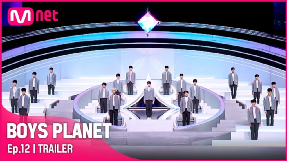 Boys Planet Episode 12 trailer screenshot showing twenty-four trainees in matching gray outfits standing on the iconic white circular elimination stage with Mnet logo and futuristic lighting setup