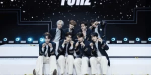 YUHZ Chinese partnership announcement photo featuring eight-member K-pop boy group in matching navy blazers and white pants posing confidently in modern studio setting with dramatic lighting and YUHZ logo backdrop